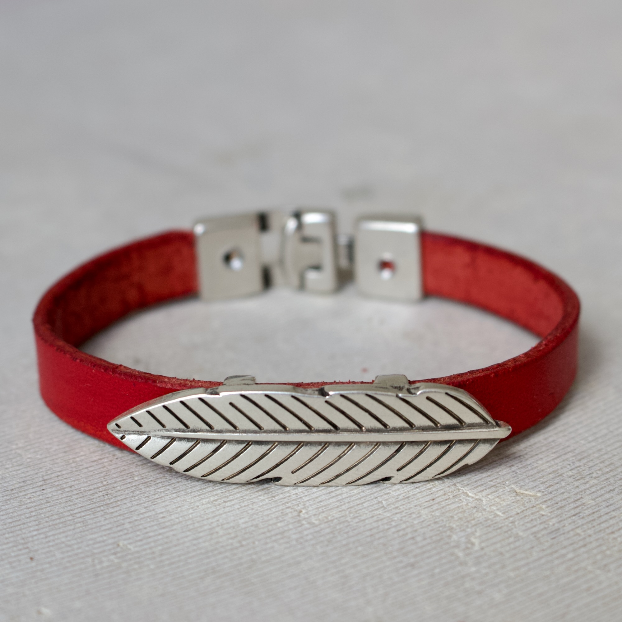 detail-bracelet-cuir-rouge-ornement-feuille Détail d’un bracelet artisanal en cuir rouge avec ornement feuille en métal argenté